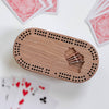 Wooden cribbage board with pegs on a white surface with playing cards.