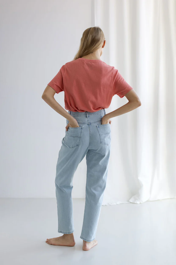 Person wearing a pink shirt and light blue pants standing in a bright room with white curtains.