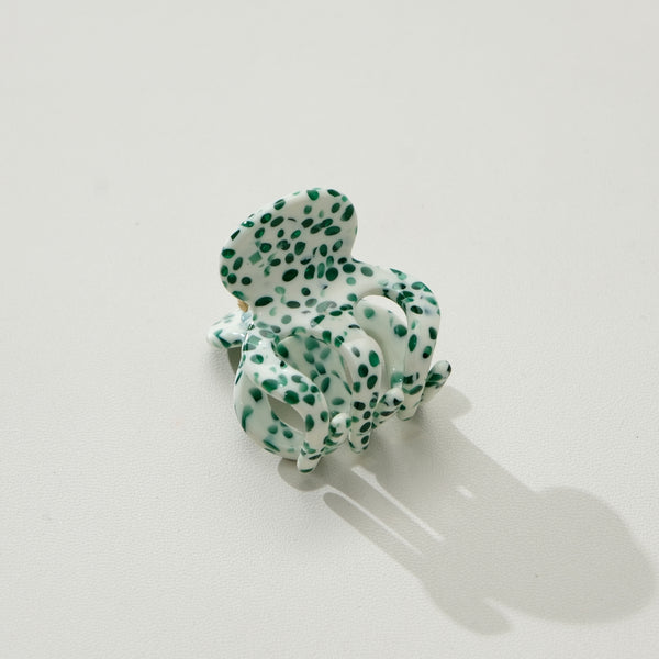 Green and white polka dot mini hair claw on a light gray background