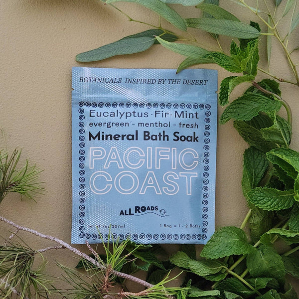 Pacific Coast Mineral Bath Soak packet surrounded by greenery on a beige background