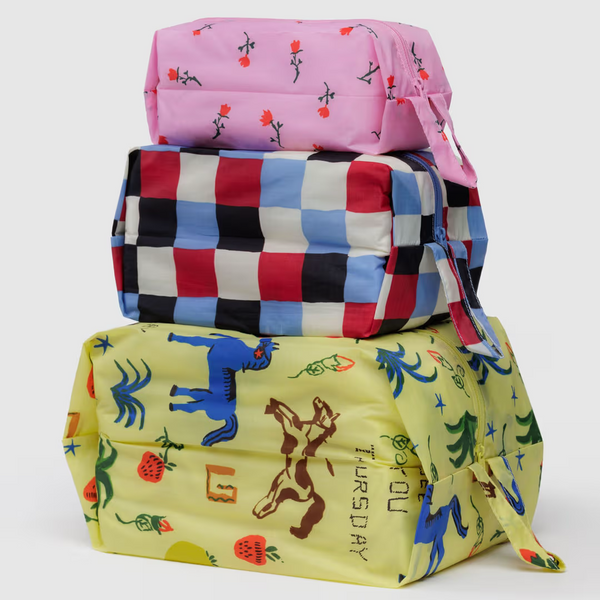 Three stacked expanding packing cubes featuring three different prints of pink flowers, a colorful mix of checkerboard, and a prairie inspired horse print.