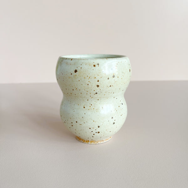 Speckled off-white ceramic cup on a light gray background