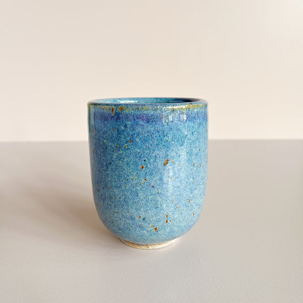 Blue ceramic cup with speckled texture on a light beige background