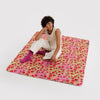 Person sitting on a colorful strawberry blossom patterned mat against a white background