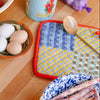 Colorful patchwork print pot holder on a wooden table with food items.