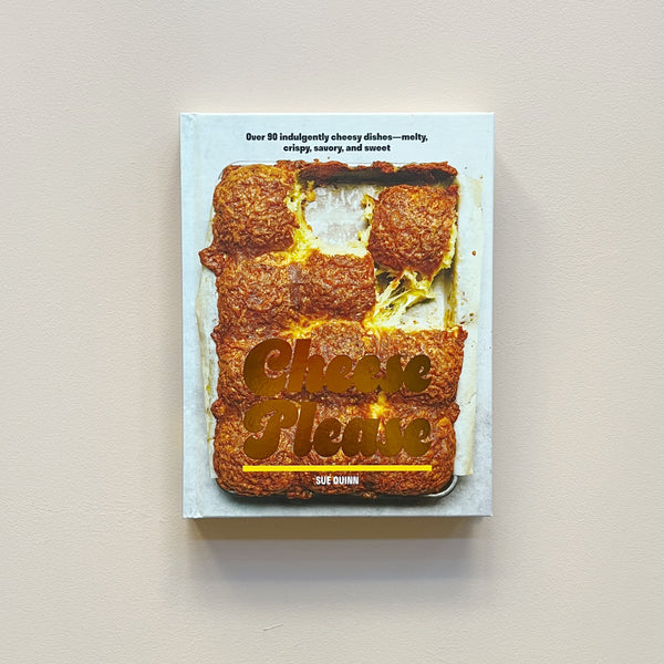 A cookbook called "Cheese Please" by Sue Quinn showing a cripsy oven-roasted dish on  a white cover. The book sits against a neutral backdrop.