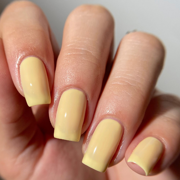 Hand with light yellow nail polish on a plain background