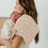 Woman holding a baby wrapped in a pink blanket against a pink goose print burp cloth against a white background.