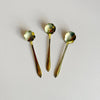 Three small gold toned metal tea spoons engraved with decorative floral designs against a neutral background.