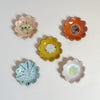 Set of five colorful mini ceramic flower-shaped dishes on a light gray background