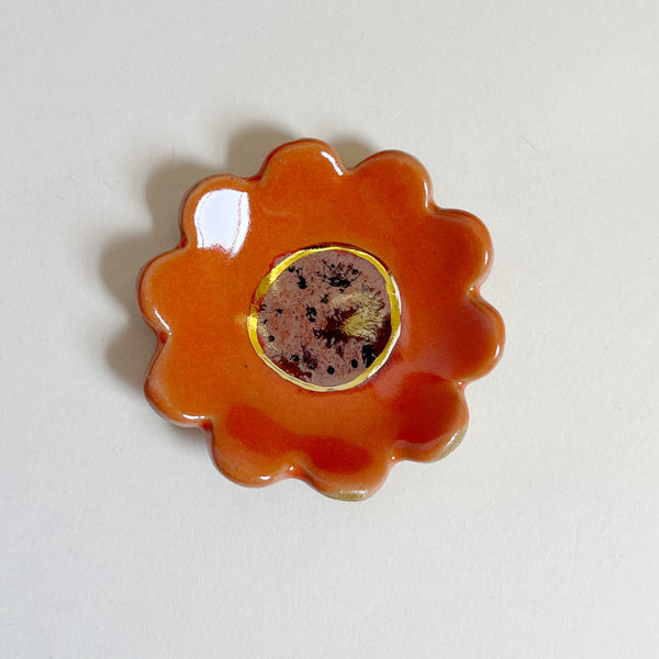 Red flower-shaped mini ceramic with a textured center on a light gray background