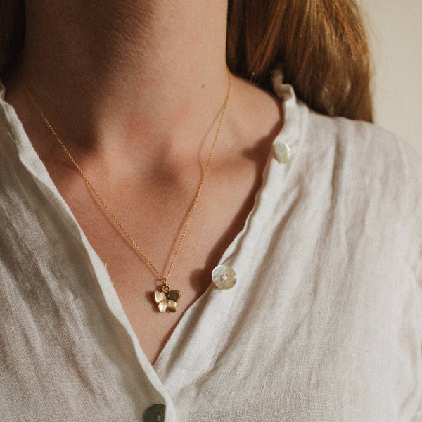 Close-up of a person wearing a delicate necklace with a small butterfly pendant on a plain background
