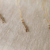 Three gold necklaces with minnow pendant designs on a textured beige surface