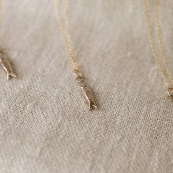 Three gold necklaces with minnow pendant designs on a textured beige surface