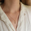 Close-up of a person wearing a gold necklace with a small bronze minnow pendant, against a neutral background.