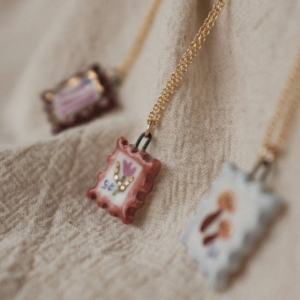 Necklaces with a small porcelain postage stamp pendants on a soft beige surface