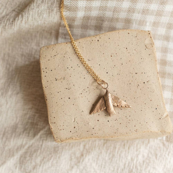 Bronze swallow pendant necklace with a gold chain on a beige stone surface