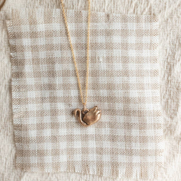 Gold necklace with a bronze swan pendant on a textured fabric background