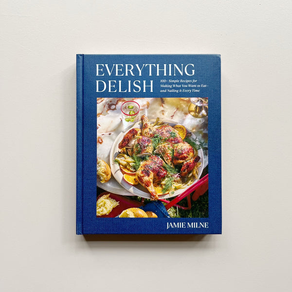 A dark blue cookbook called "Everything Delish" by Jamie Milne against a neutral background.