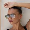 Woman wearing gold sunglasses and hoop earrings with a neutral background