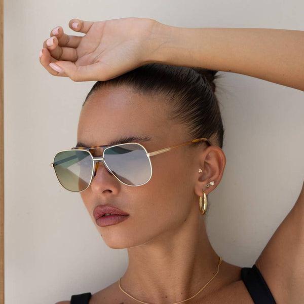 Woman wearing gold sunglasses and hoop earrings with a neutral background