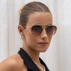 Woman wearing gold sunglasses with a neutral background