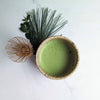 Ceramic bowl with green matcha, a whisk, and greenery on a white background