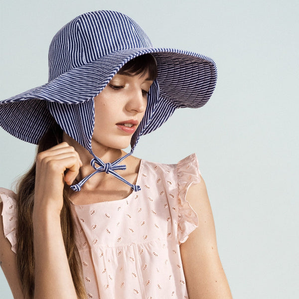 Woman wearing a blue and white striped sun hat against a light gray background