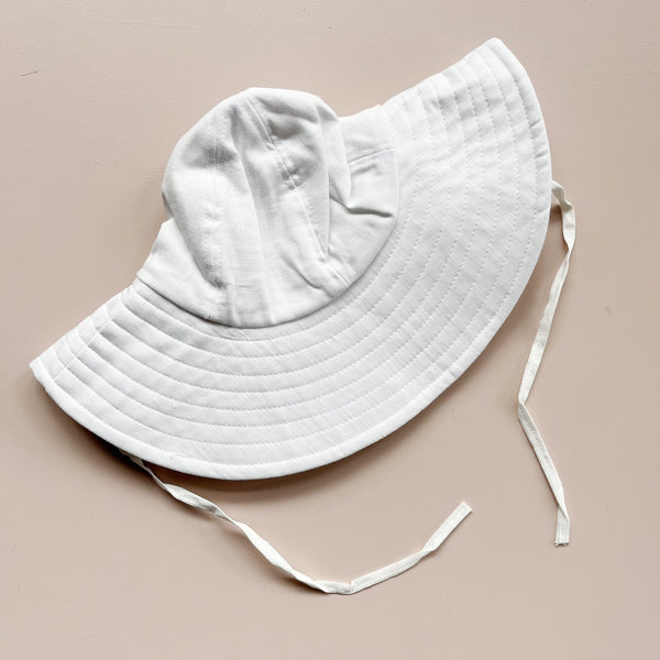White sun hat with a ribbon tie on a beige background