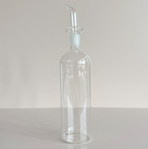 Clear glass bottle with a long spout on a light gray background