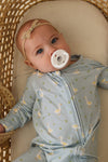 Baby wearing a light blue outfit with geese pattern, lying in a wicker crib.