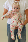 Baby in a cherry print onesie being held by an adult against a plain background