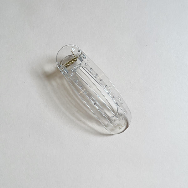 Clear lay-flat hair claw on beige background.