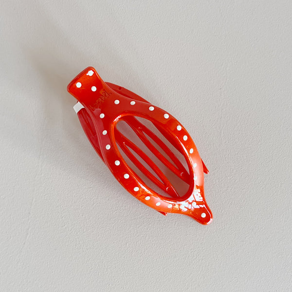 Red hair clip with white polka dots on a light gray background