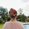 Person wearing a red and white polka dot hair clip in front of an outdoor pool and trees.