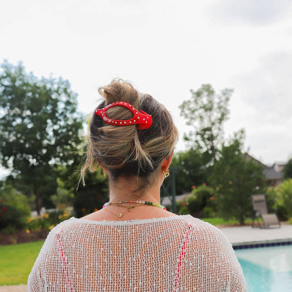 Person wearing a red and white polka dot hair clip in front of an outdoor pool and trees.