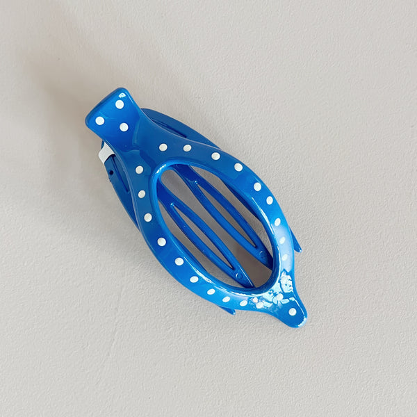 Blue hair clip with white polka dots on a light gray background