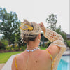 Person wearing a yellow and blue polka dot hair claw in front of an outdoor pool and trees.