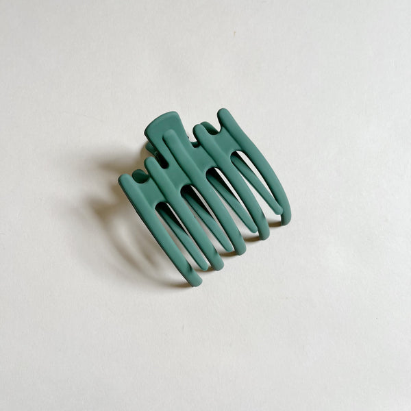 Matte dark green lay-flat hair claw on beige background.