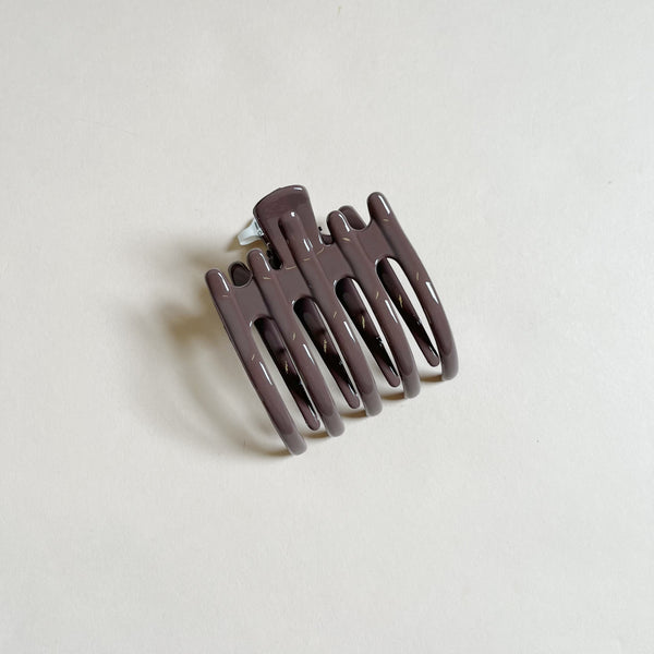 Shiny purple-brown lay-flat hair claw on beige background.