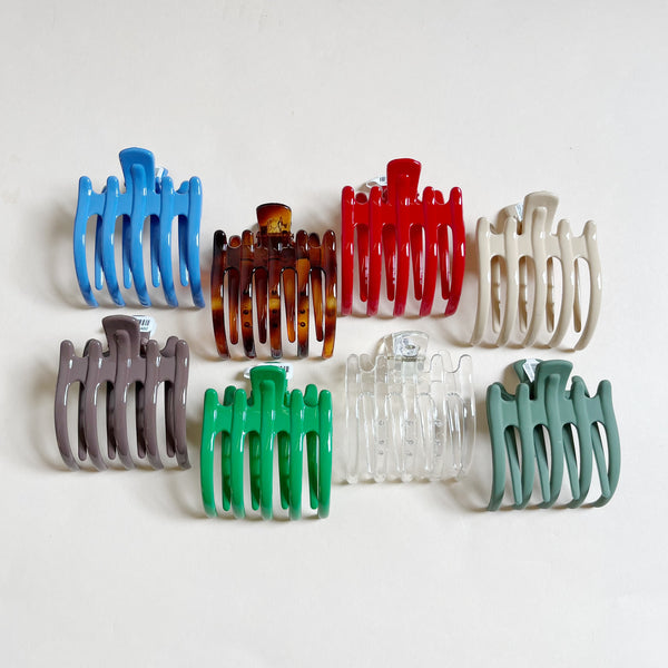 Assortment of wide lay-down claw hair clips on a beige background.