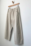 Beige pants hanging on a wooden hanger against a white wall