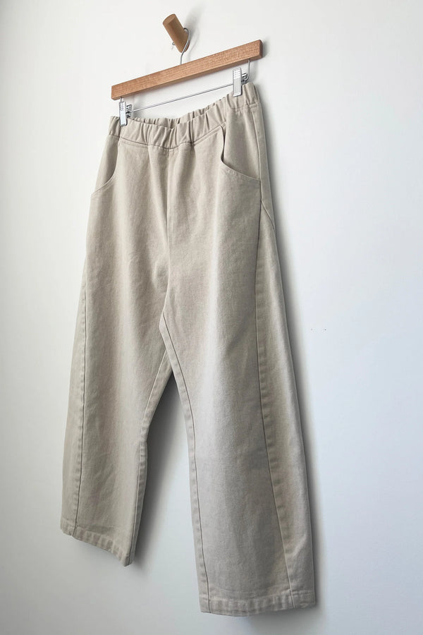 Beige pants hanging on a wooden hanger against a white wall