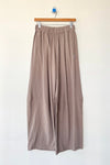 Beige wide-leg pants hanging on a wooden hanger against a white background