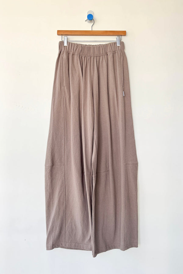 Beige wide-leg pants hanging on a wooden hanger against a white background