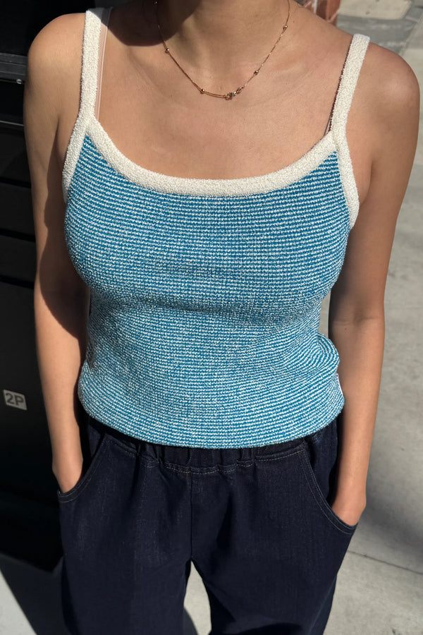 Person wearing a blue tank top with white trim on a street background