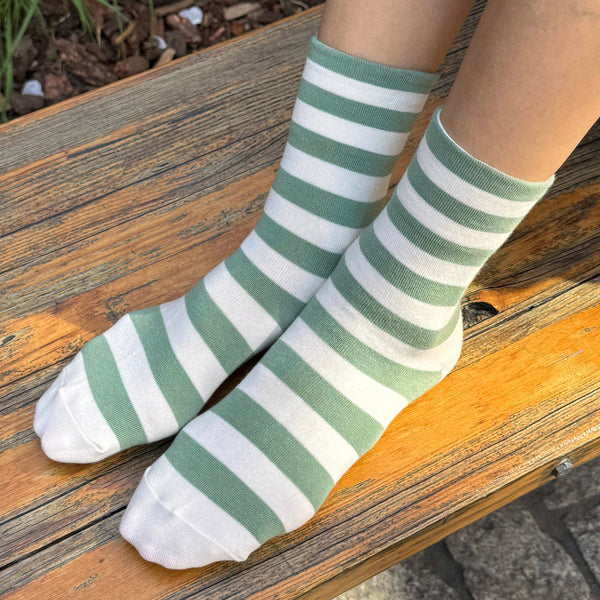 Green and white striped socks worn on a wooden bench.