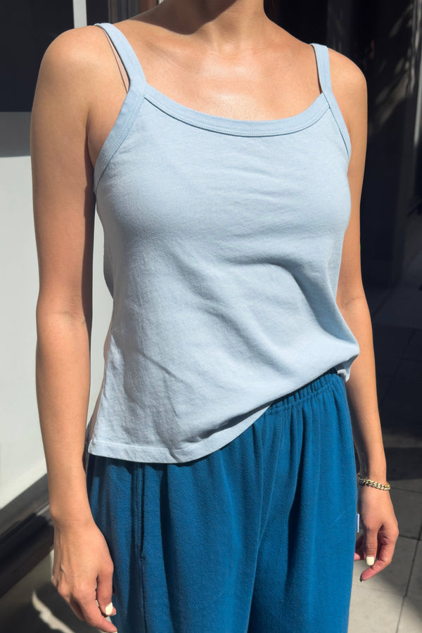 Person wearing a light blue tank top and blue pants indoors.