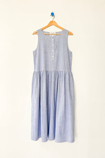 Blue and white striped cotton sleeveless dress on a wood hanger against a white wall.