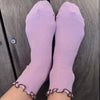 Purple socks with brown ruffled cuffs on a wooden floor